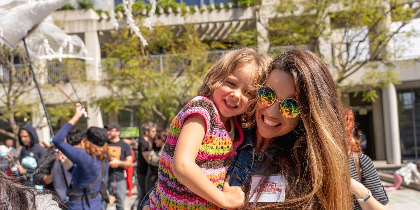 Mother holding young daughter dancing and smiling outside during a festival