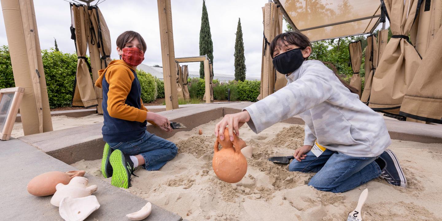 2 children uncovering objects buried in sand