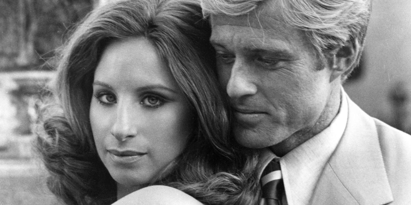 Still from the film showing Streisand and Redford standing together. She is looking at the camera and he is looking down.