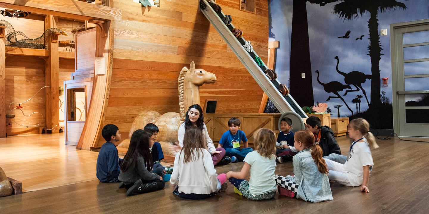 A group of young students sitting in a circle with an adult at the entrance to Noahs Ark