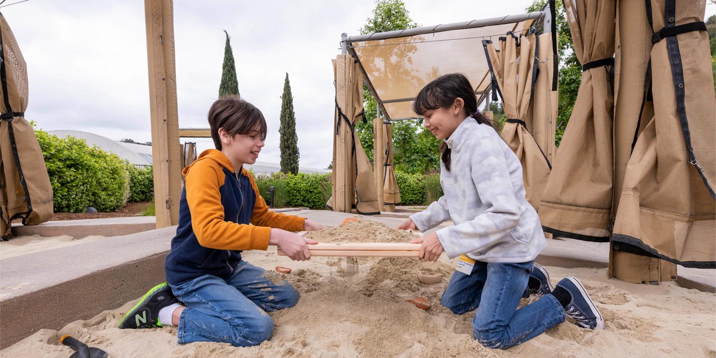 Two children uncovering objects buried in sand