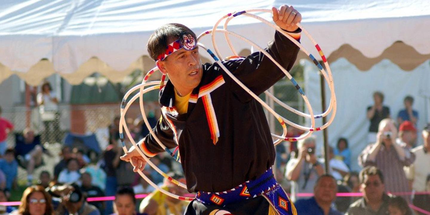 Photo of a man performing outside with numerous hoops moving around his arms