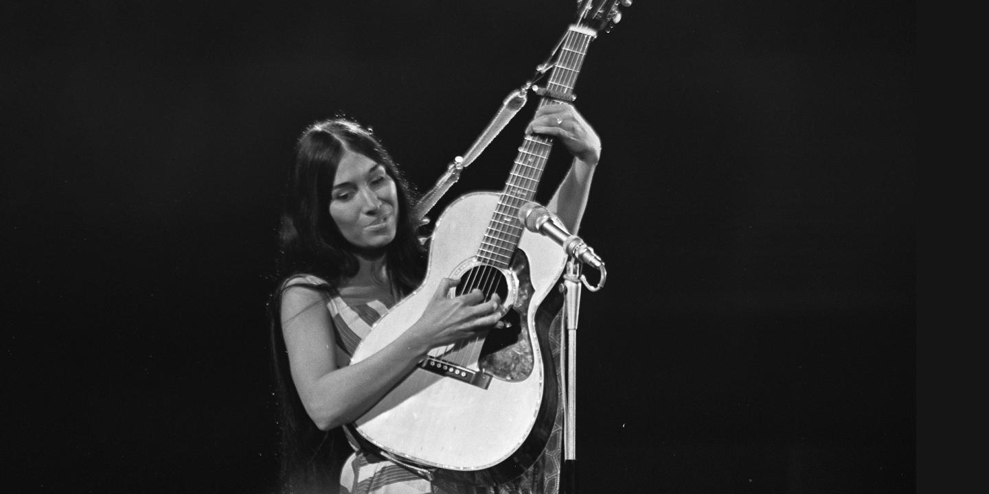 Buffy Sainte-Marie, musician, pictured playing an acoustic guitar in black and white