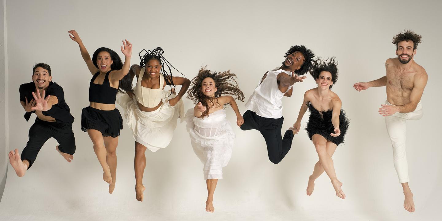 Seven dancers all facing forward and leaping into the air