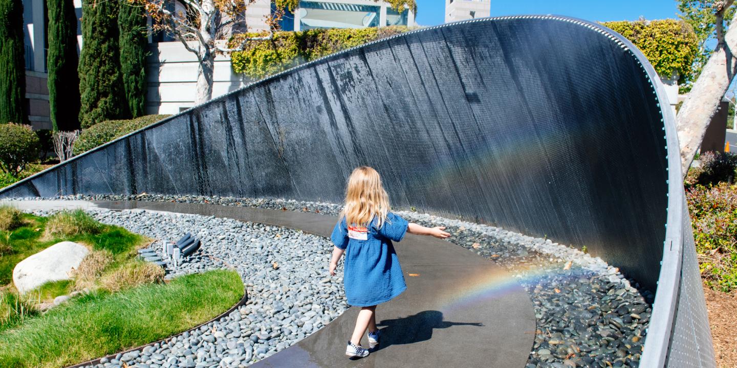 A little girl walks through the rainbow mist arbor as rainbows appear in the mist.