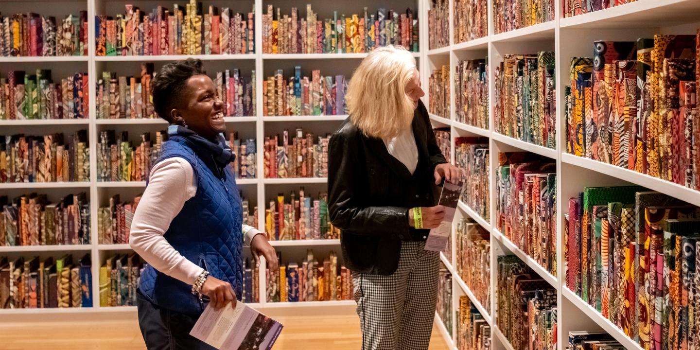 Two people looking at colorful books on a bookshelves in a gallery.