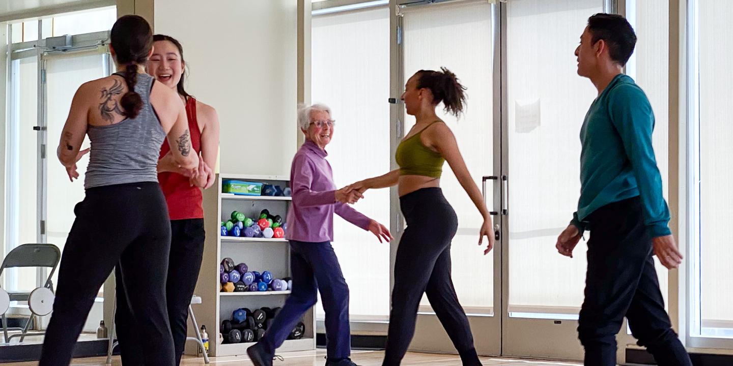 Five people of different ages, ethnicities, and genders dancing together in an exercise studio