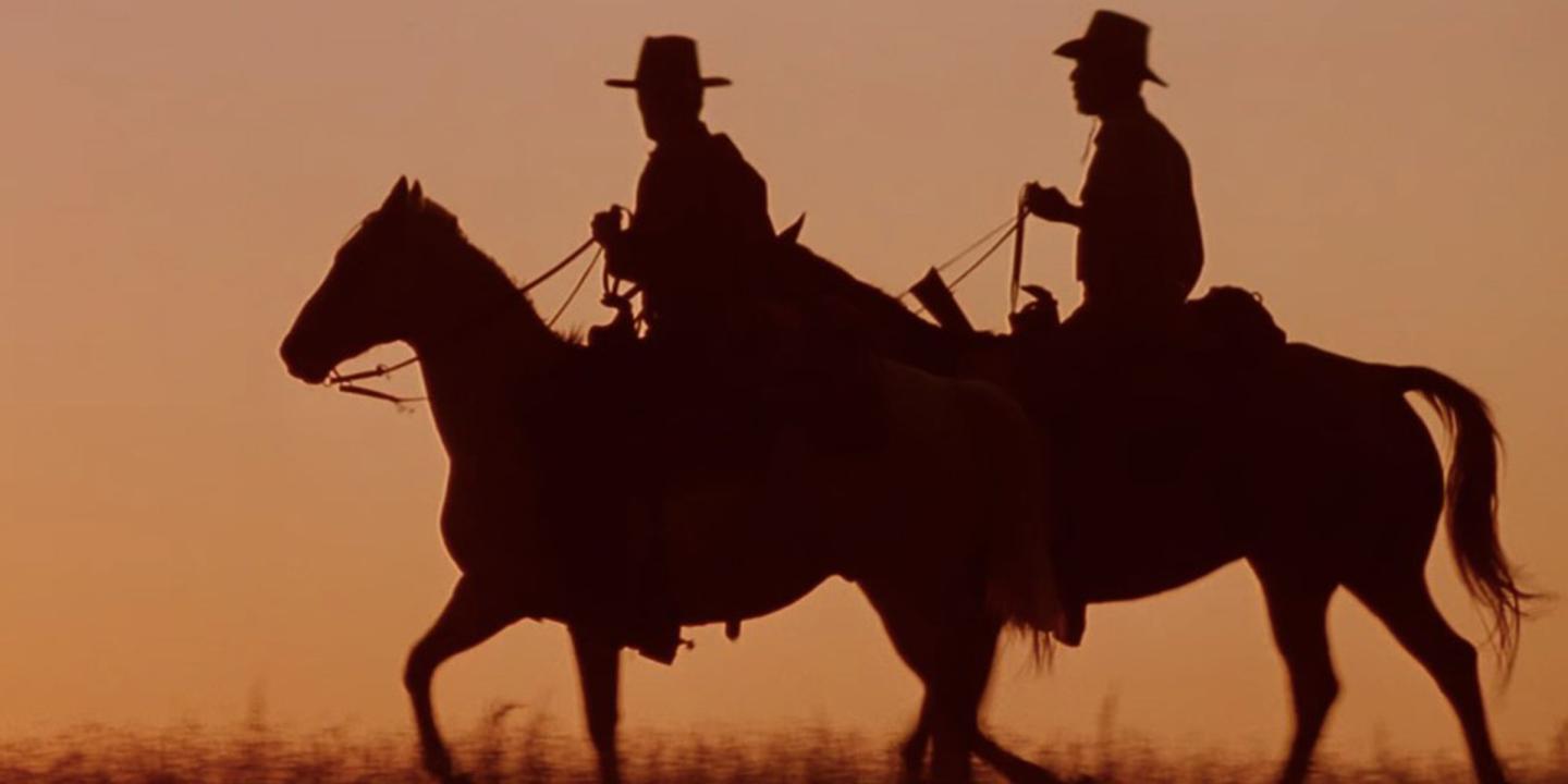 Silhouette of two cowboys riding horses against an orange sunset