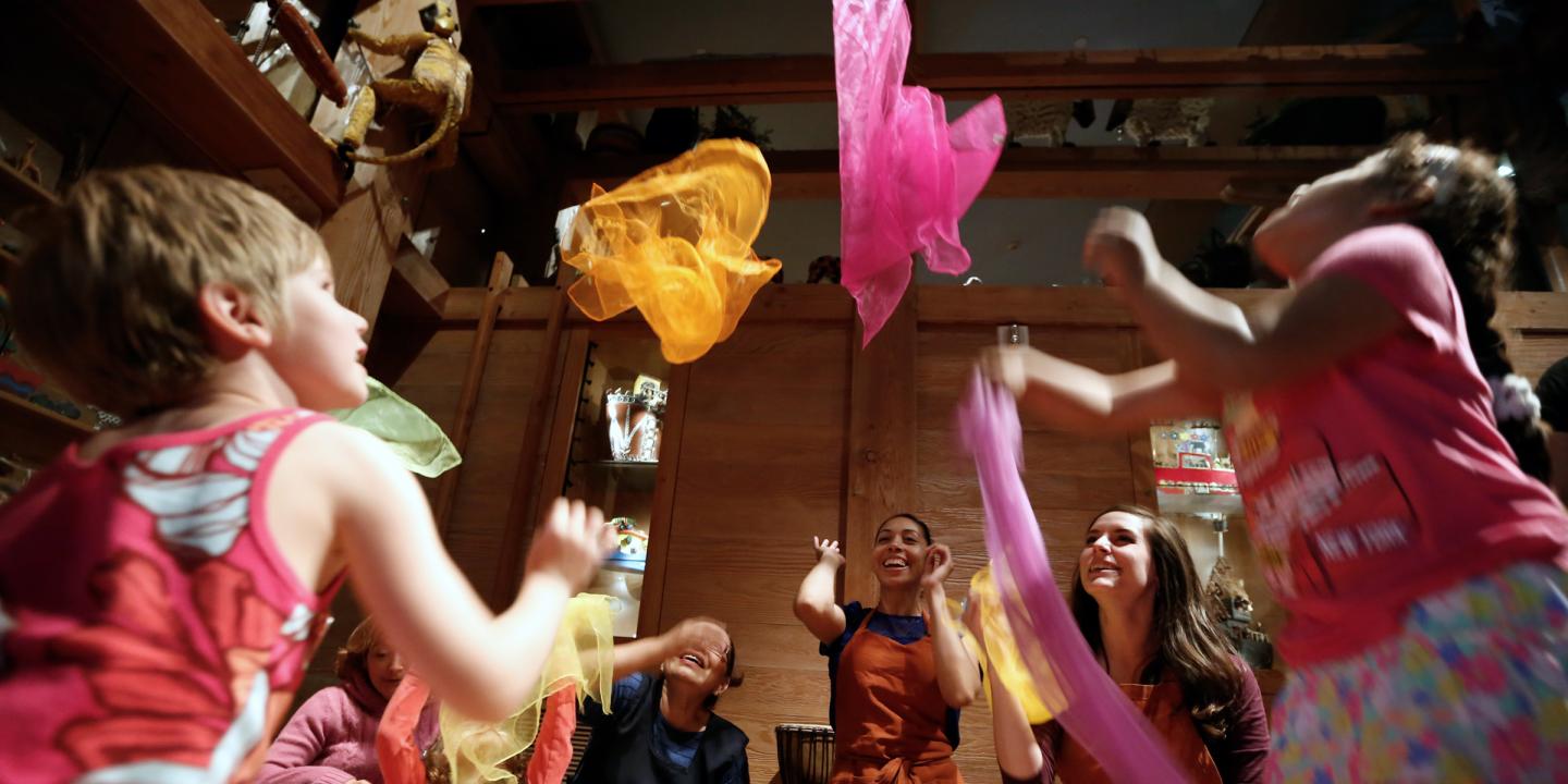 A group of young children throwing colorful scarfs in the air and dancing around.