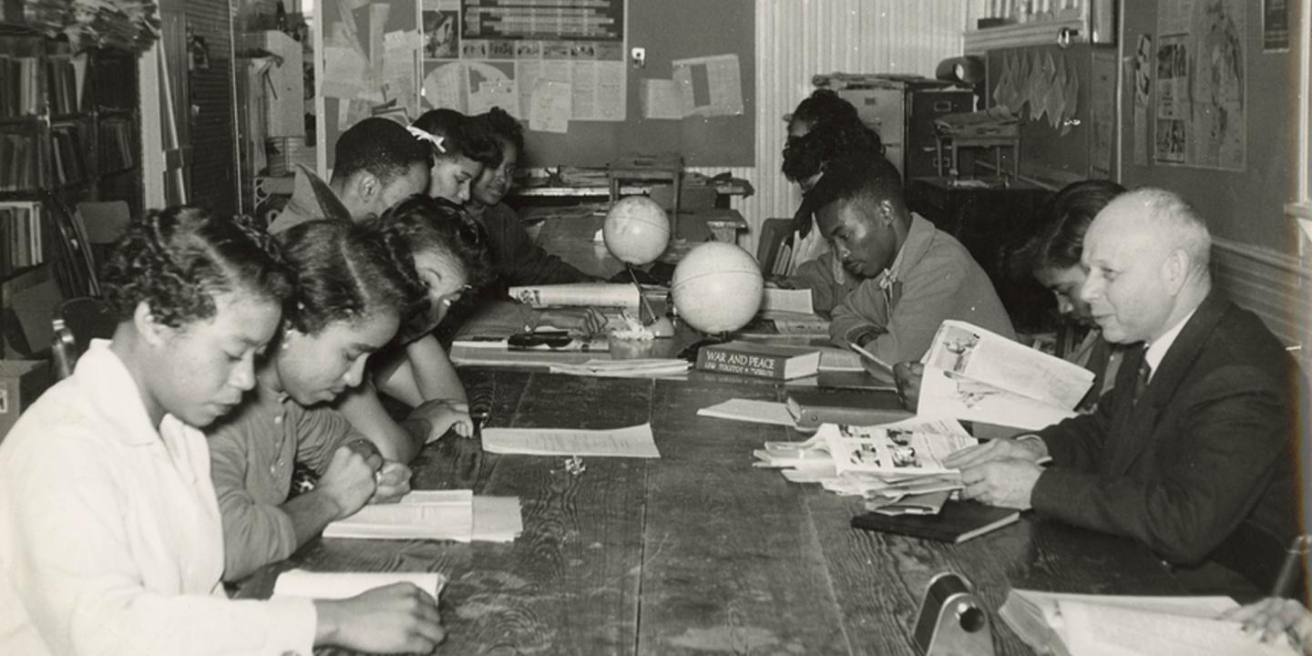 A black and white historic photo of a college scholar sitting at a table with black college students