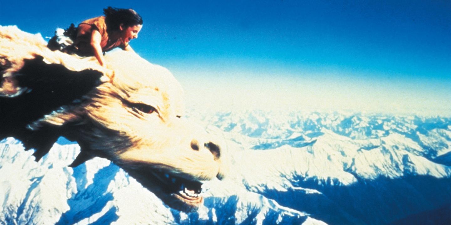 Still from the movie The NeverEnding Story showing the main character, Bastian, riding over snow capped mountains on the dragon Falkor.