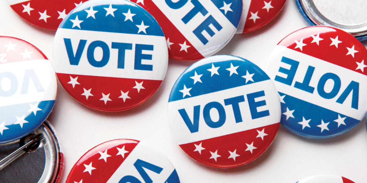 On a white table sits a collection of red, white, and blue buttons with the word Vote and stars printed on them.
