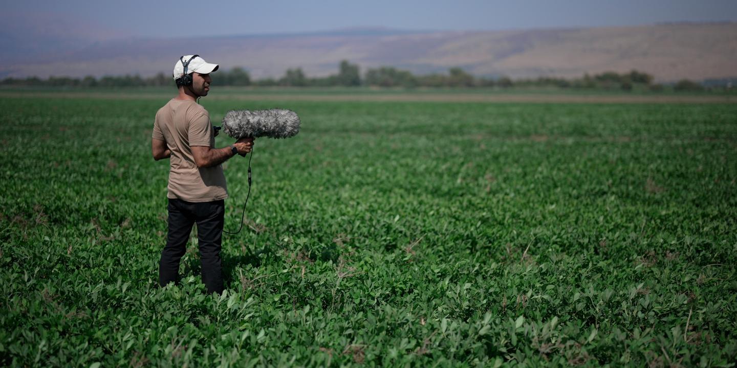 A man with a large microphone stands in the middle of a vast green field