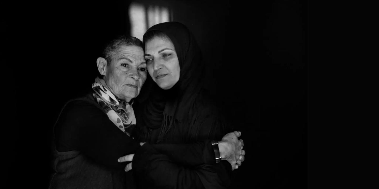 Black and white photograph of two women holding each other with sad, solemn expressions.