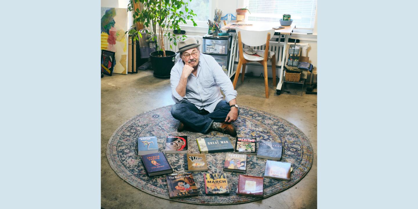 Dr. David Greenfield looking at the camera while sitting on a rug beside a collection of graphic novels and comic books on display.