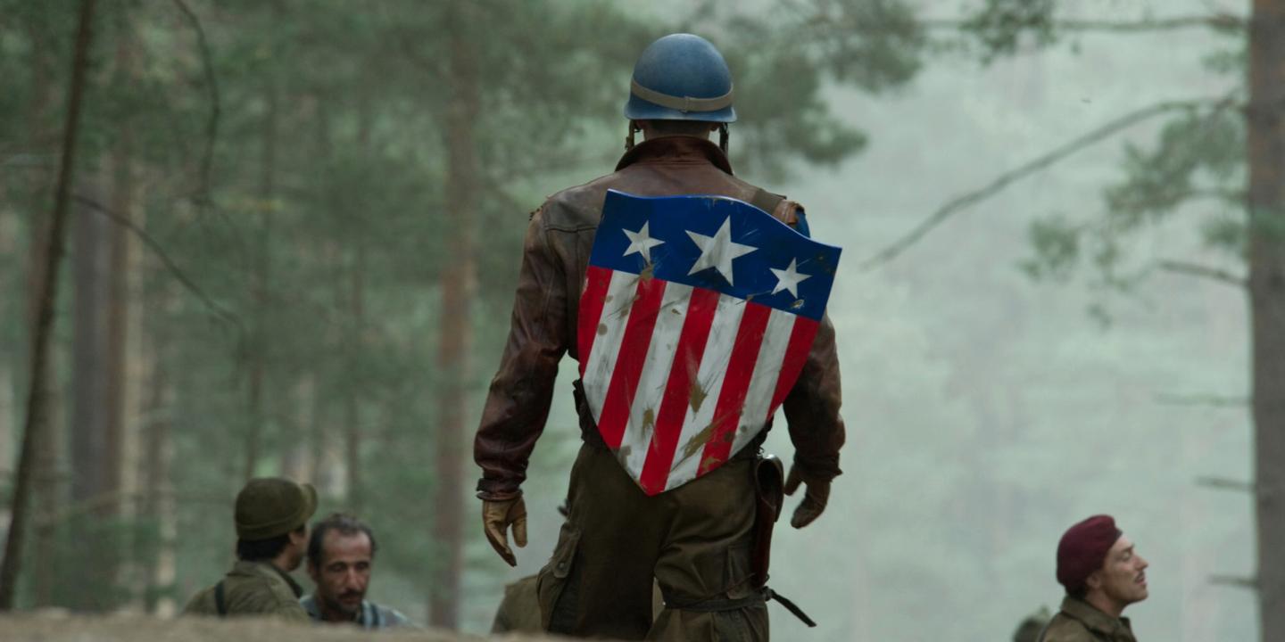 Still from the film showing Captain America walking towards a group of soldiers in a field wearing the iconic Stars and Stripes shield on his back.