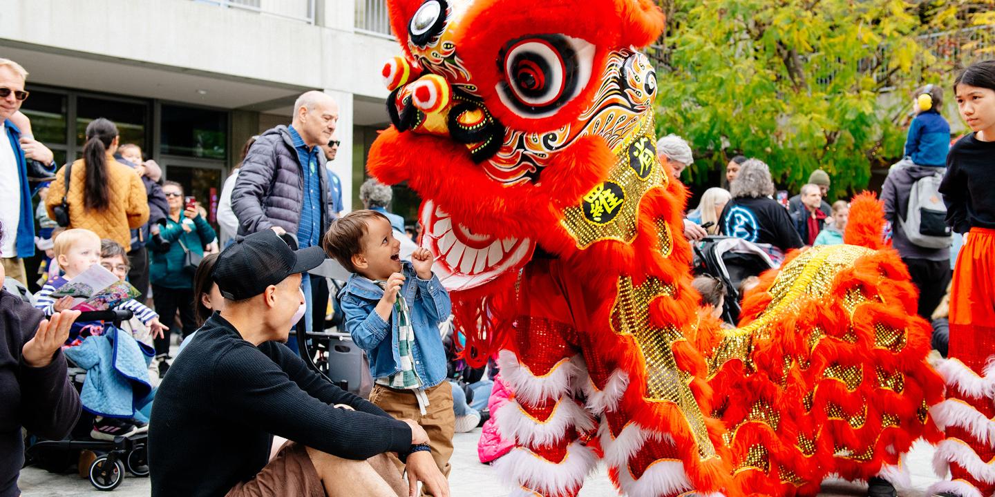 A child stares excitedly at a red dragon puppet in the courtyard.