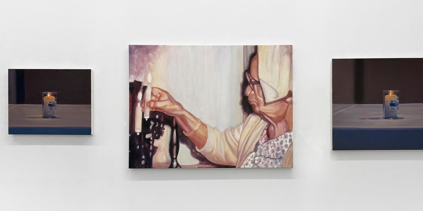 Three paintings on a gallery wall depicting candles with the one in the middle a person lighting one.