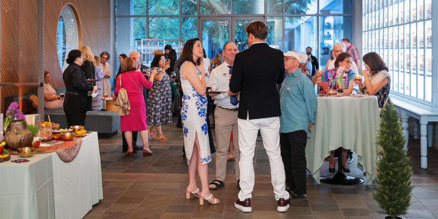 A room of people talking in small groups with appetizers and drinks.