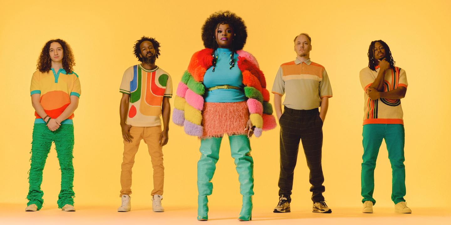 A band with five members pose with colorful outfits.