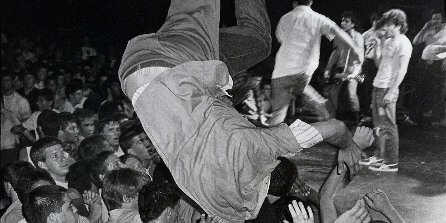 A man stage dives into a crowd of people at a concert.