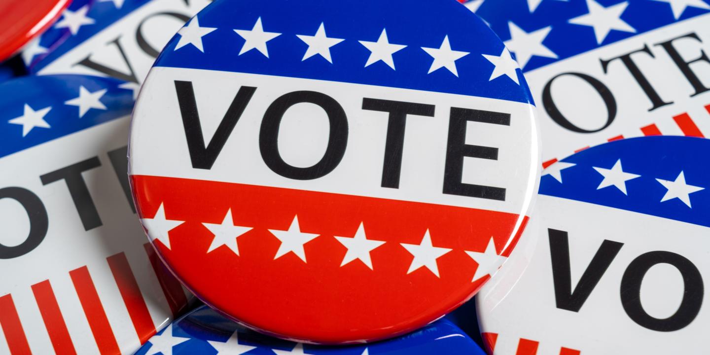 A close up of red, white and blue pins that say "vote".