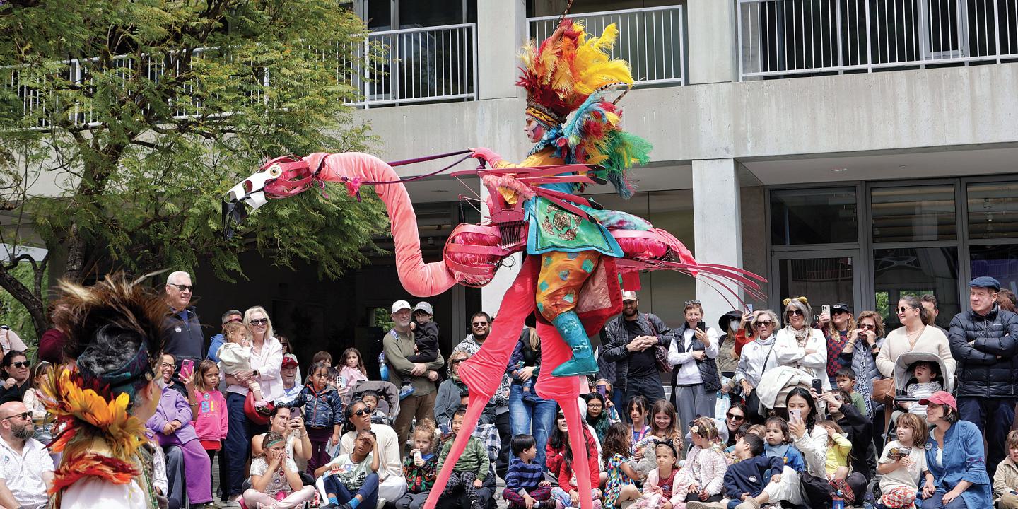 A puppeteer rides a flamingo puppet through Taper Courtyard.