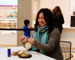 A woman seated at a table with plate of potato pancakes and a cookie shaped like a dreidel