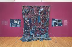 sculpture made of clothing pieces hanging on exhibit wall