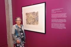 woman standing next to a painting hanging on exhibit wall