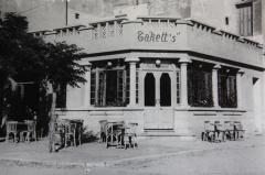 Photo of exterior a building with a sign that says 'Takett's' with tables and chairs on the sidewalk in front