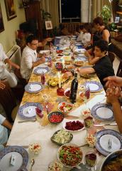 people seated at a long rectangular dining table with plates of food and wine and candles on the table