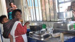 a woman cooking with a baby on her back