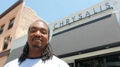 a man standing in front of a building with a sign, 'Chrysalis'