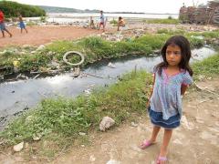 a young girl standing next to a creek with garbage in and around it