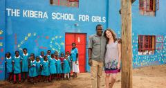 a man and woman pose outside a school with a group of young girls and a teacher standing behind them