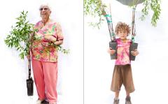 on older woman holding a small pomegranate tree in a pot and a young child holding 2 small pomegranate trees in pots