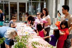 adults and children standing and sitting around a table writing and drawing on pieces of paper