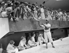 people in grand stand above dugout; one person handing papers to Jackie Robinson who is standing in front of the dugout
