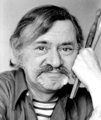 close-up photo of a man with a mustache holding 2 paint brushes