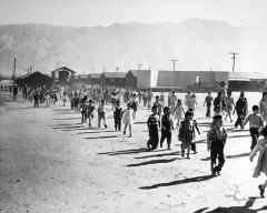 children walking down a dusty dirt road with barracks visible in distance behind them