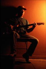 Paul Simon in cap seated on a chair playing guitar