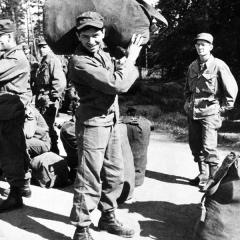 Bill Graham in military fatigues carrying a large duffle bag on his shoulder