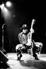 Bo Diddley crouching down on a stage holding a guitar upright