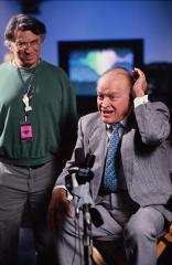 Bill Graham standing next to a seated Bob Hope with microphones in front of him