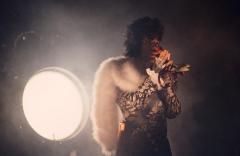 Prince wearing a fur stole backlit by a large circlular light