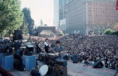 a band on an outdoor stage with a huge crowd of people that stretches into the distance