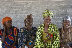 4 women seated in a row in front of a chalkboard with writing on it