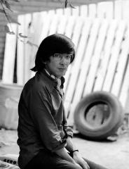 Black and white photo of Tamio Wakayama sitting near a house looking directly at the camera.