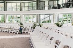 An empty ballroom filled with white chairs and flower arrangements set for a wedding.